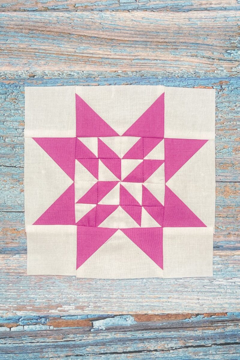 Twilight Stars QAL week 11 block 4. This block is made of half square triangles offset by flying geese and corner blocks. It is white and bright purple