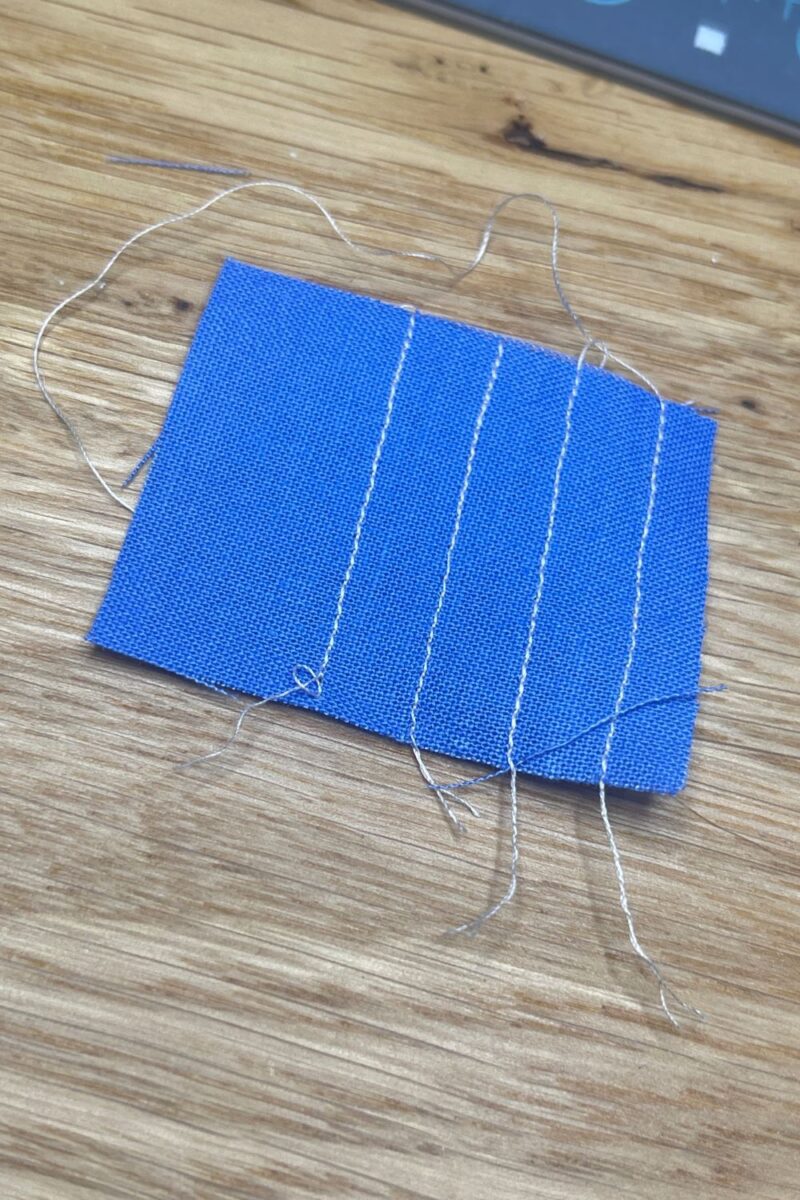 A blue piece of fabric showing multiple stitched lines after using the scrap fabric for a leader or ender piece.