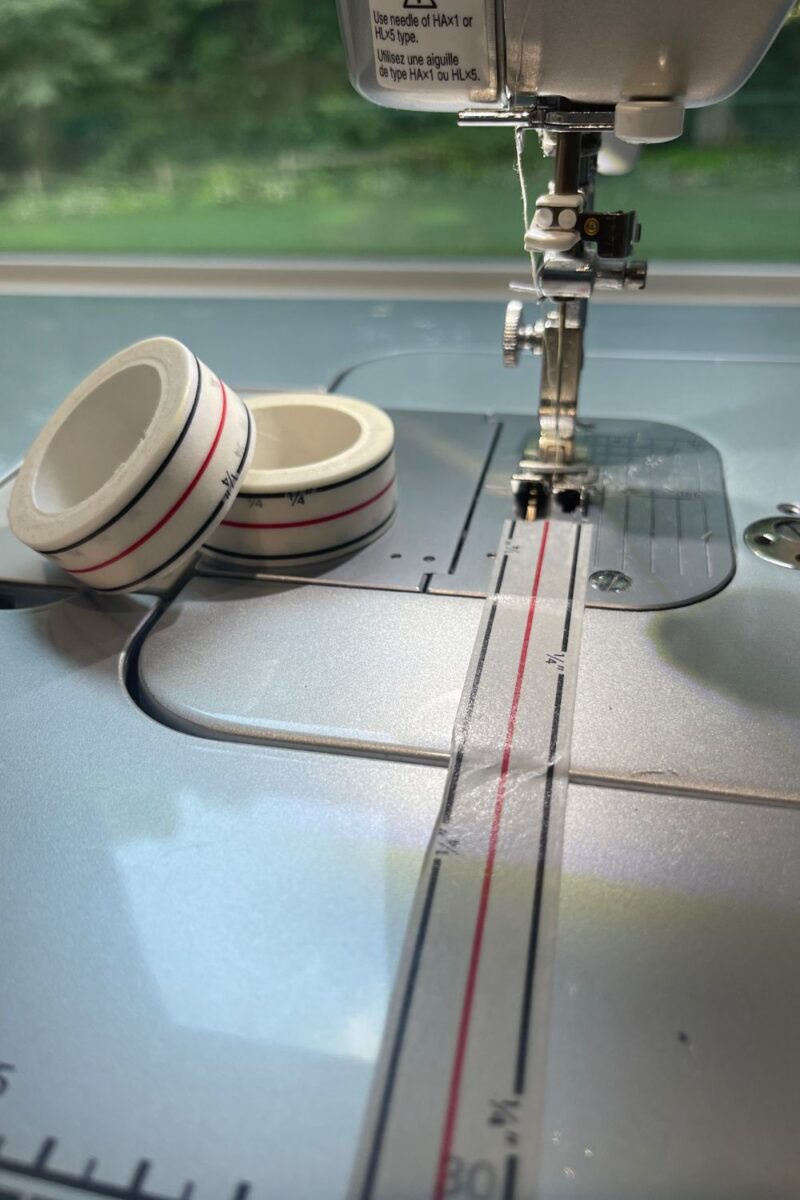 A sewing machine surface showing the use of diagonal seam tape to mark a center line and 1/4 seam allowance lines