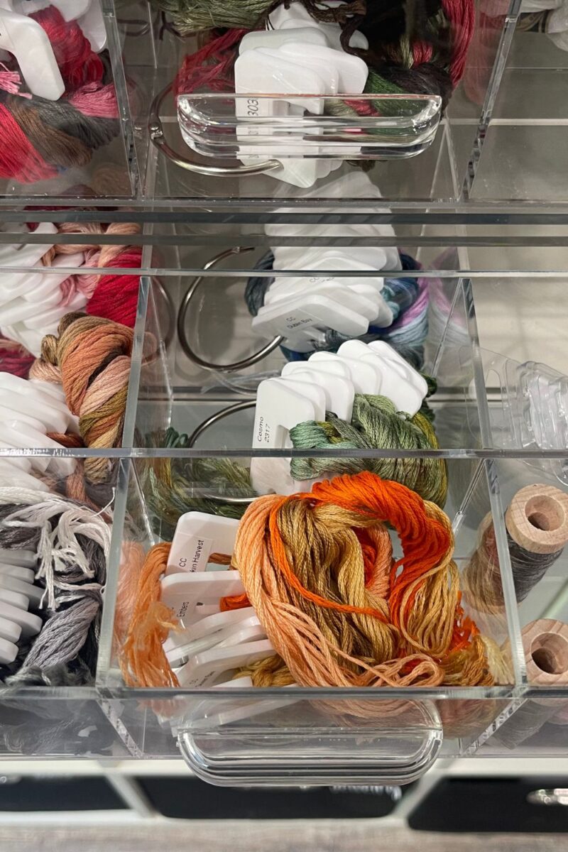DMC cross stitch floss organized on floss drops in acrylic drawer organizers.