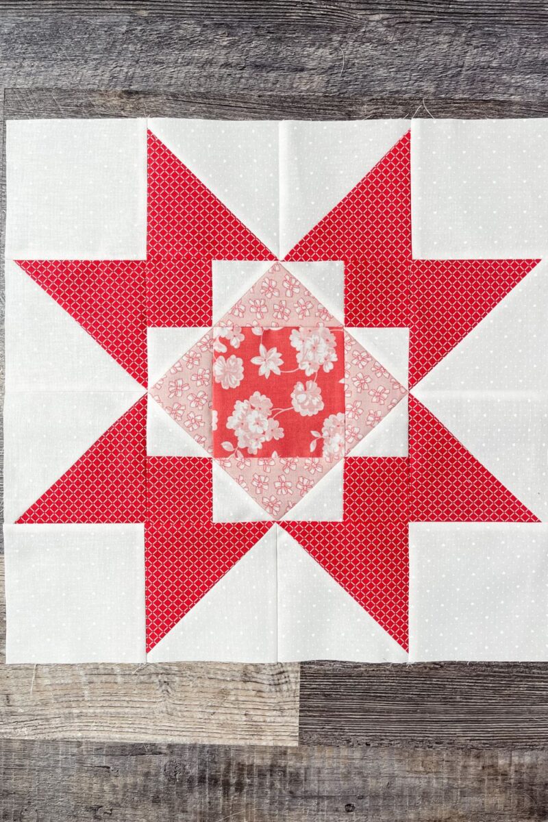 Adore quilt block 1. Red, pink, and white quilt block with a center square, flying geese, and corner posts. Set off by star points.