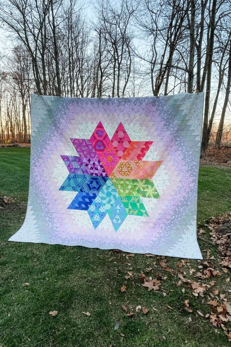 The finished nebula quilt. A rainbow medallion quilt made of triangles, hexagons, and diamond pieces.