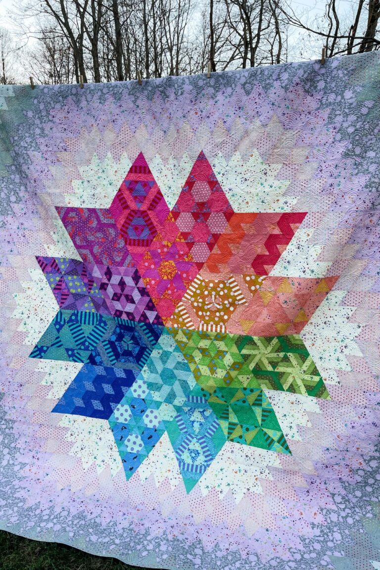 Finished Nebula Quilt. Colored diamond blocks in the center of a lighter lilac and grey background.