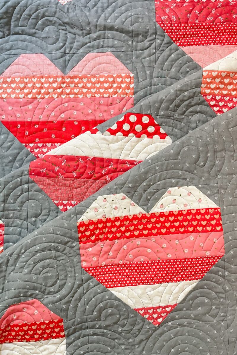 Heart quilt made with Sincerely Yours fabric in pink, red, and white. Uses Beyond Bella grey background.