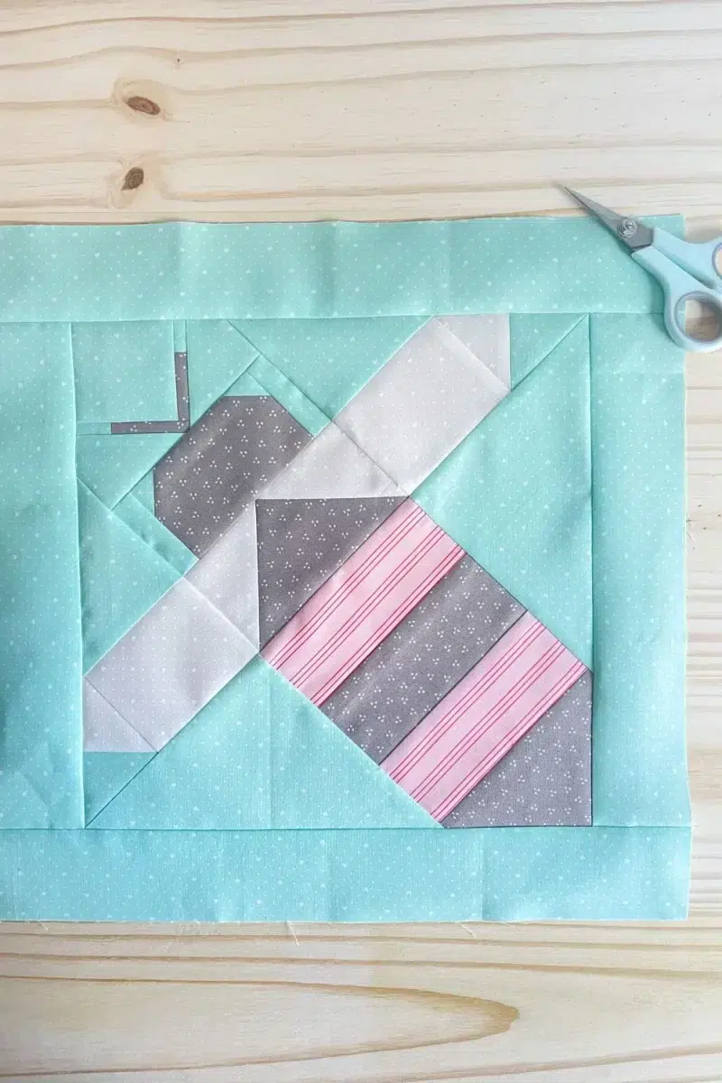 The Bee's Knees Block is a quilt block with a teal background and a traditionally pieced bee shape.