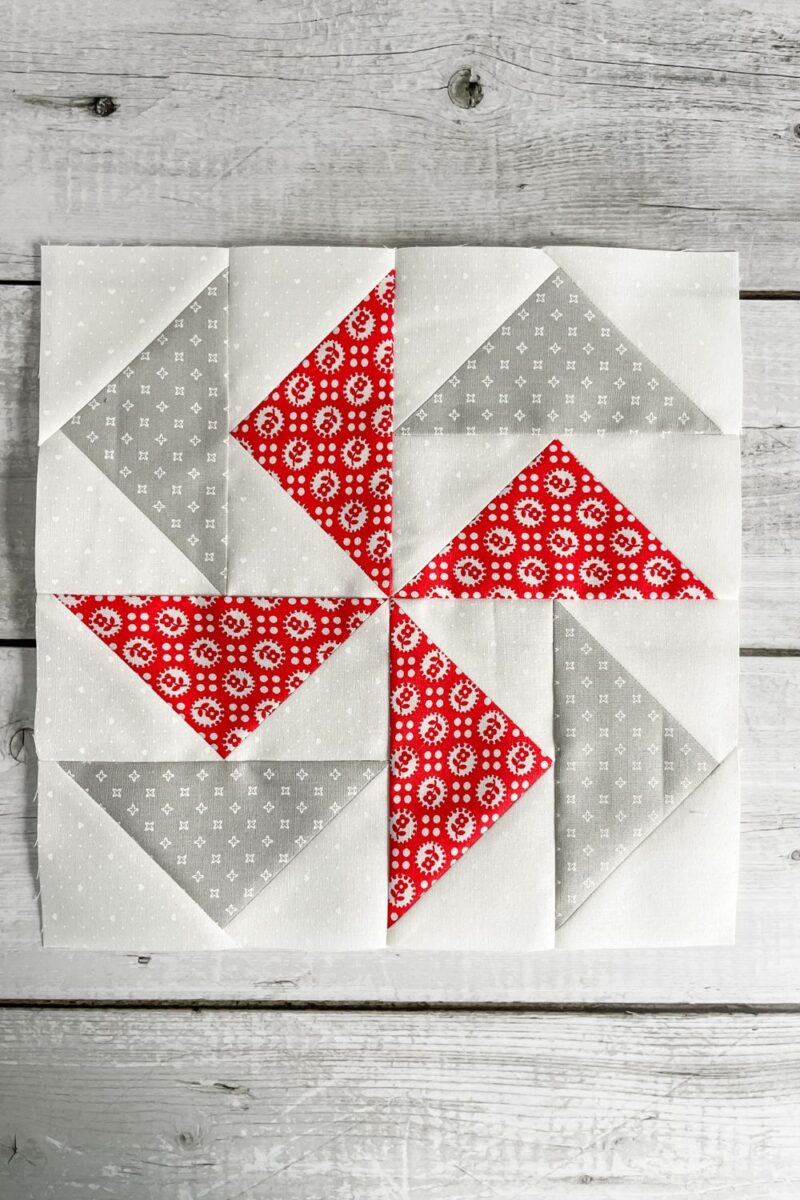 A quilt block made of 8 flying geese in a spiral arrangement of red and grey geese.