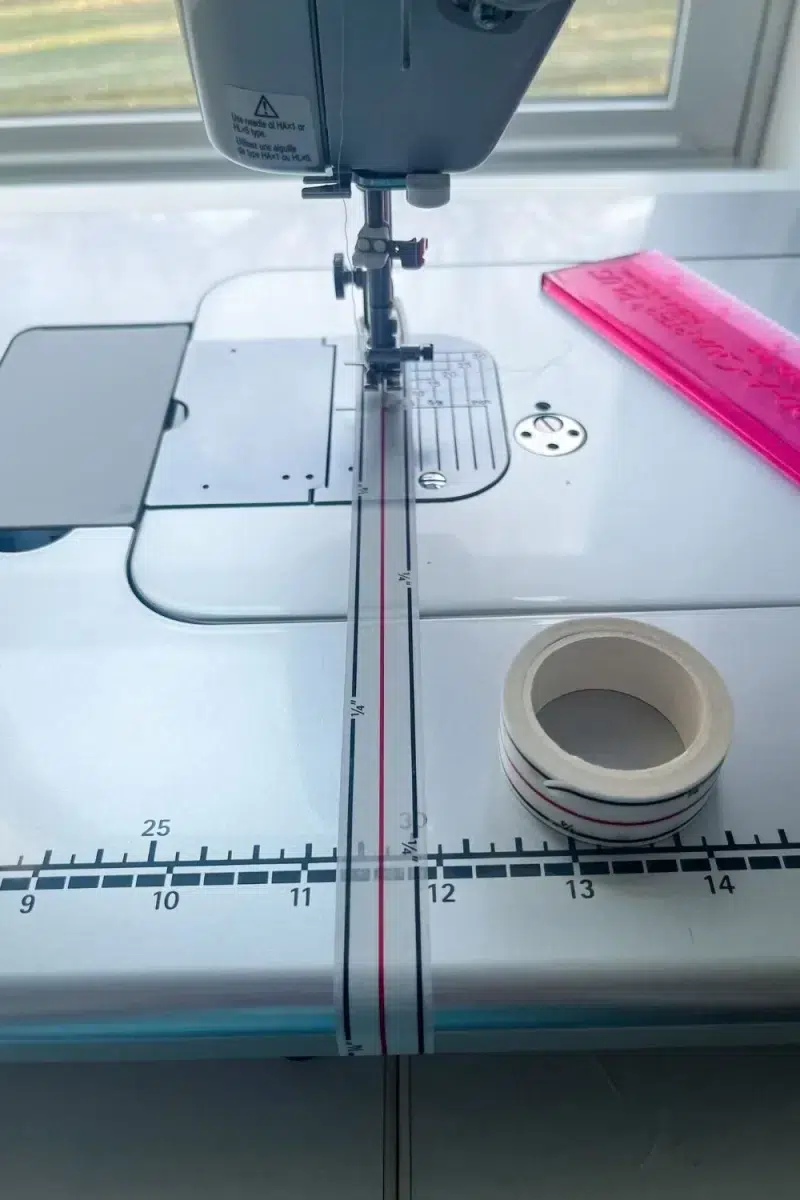 Seam tape aligned under the needle and applied down the front of the sewing machine bed.
