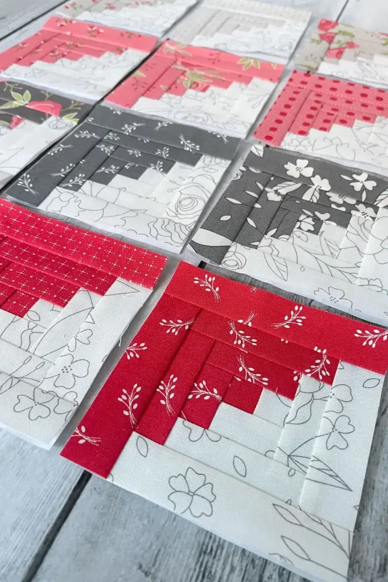 Paper pieced log cabin blocks with half of each block in a grey and white pencil sketch print and the other halves in pink, tan, dark gray, and red floral printed fabrics. This is a close up of one of the red and white quilt blocks