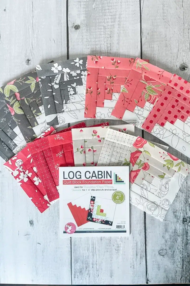 Paper pieced log cabin blocks with half of each block in a grey and white pencil sketch print and the other halves in pink, tan, dark gray, and red floral printed fabrics. 12 blocks all together.