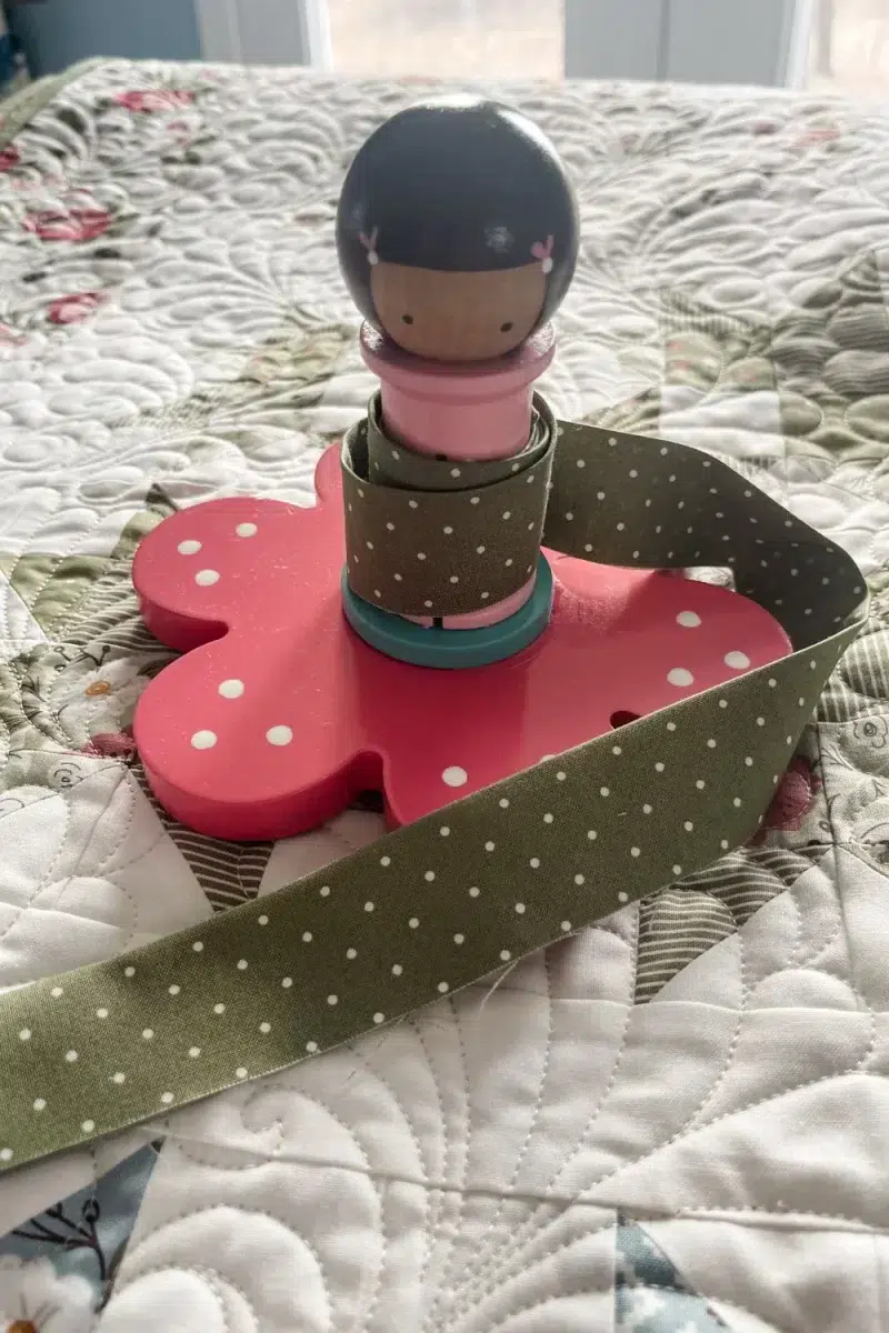Binding Babies tool with flower base. This decorative spool holds a length of binding to keep it neat during application