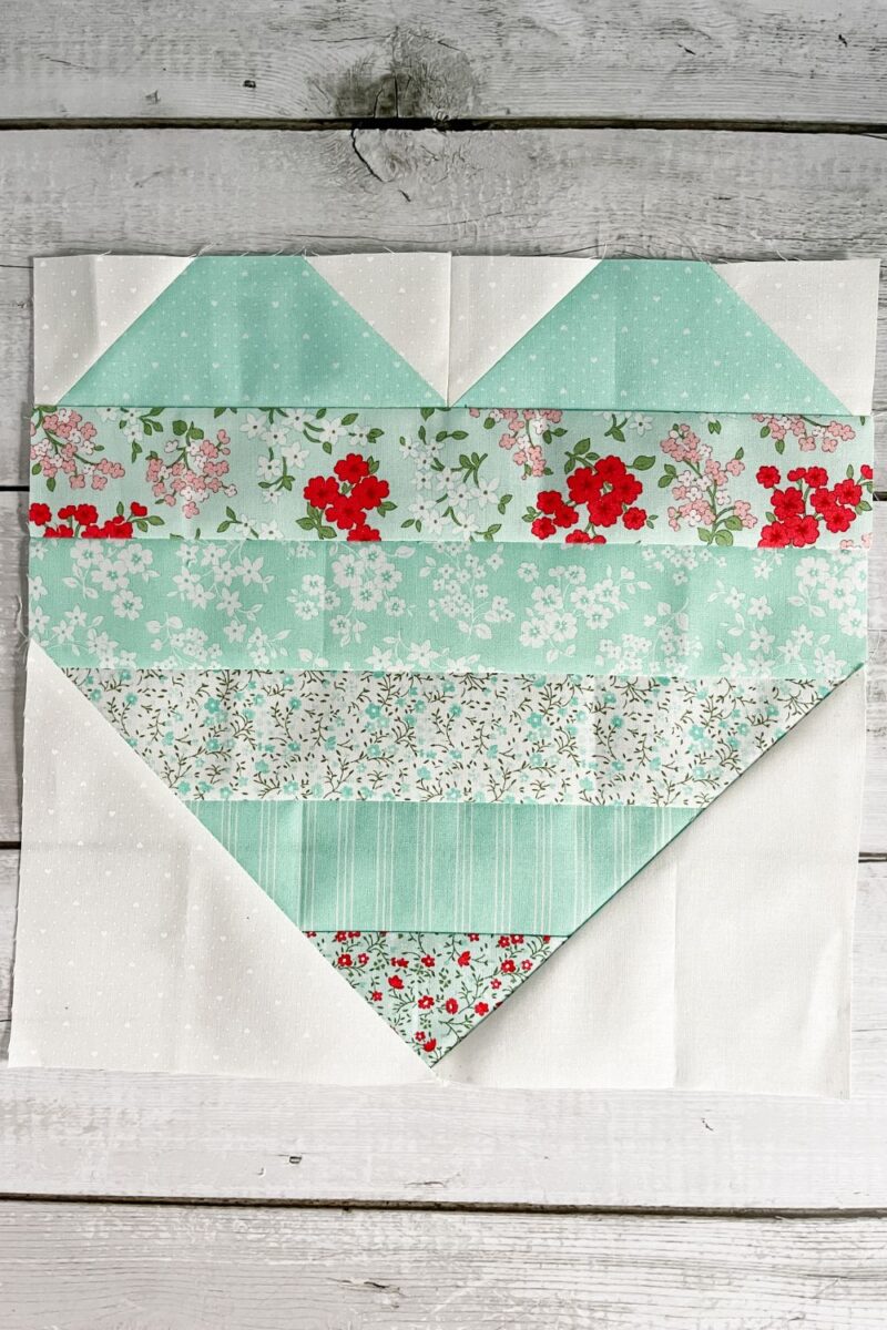A heart shaped quilt block made with aqua strips and white background print.