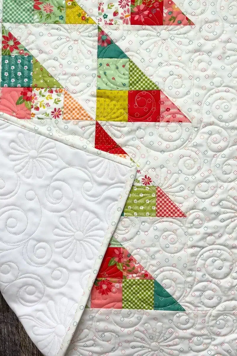 Mini charm pack quilt folded over to see the quilting stitches on the solid white backing.
