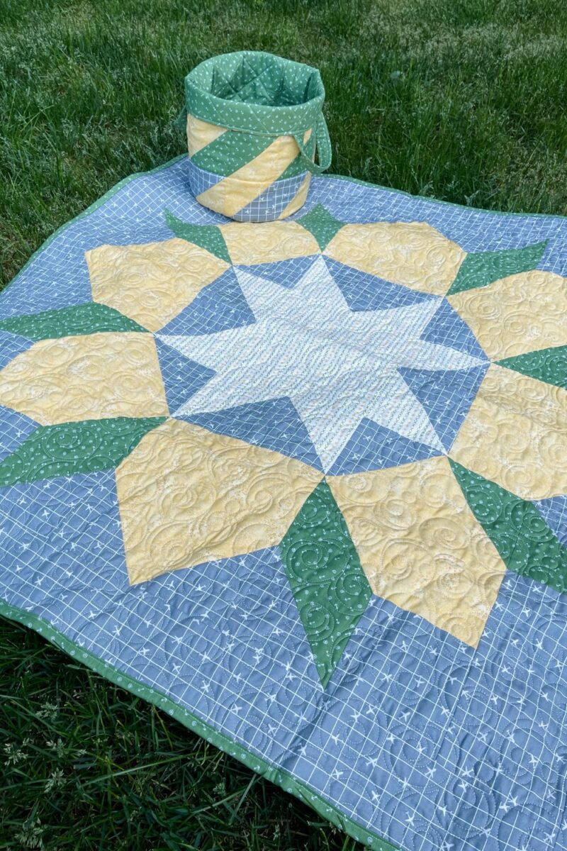 Swoon baby quilt laid out on the grass with coordinating fabric basket. Made with gender neutral prints in green, yellow, and grey.