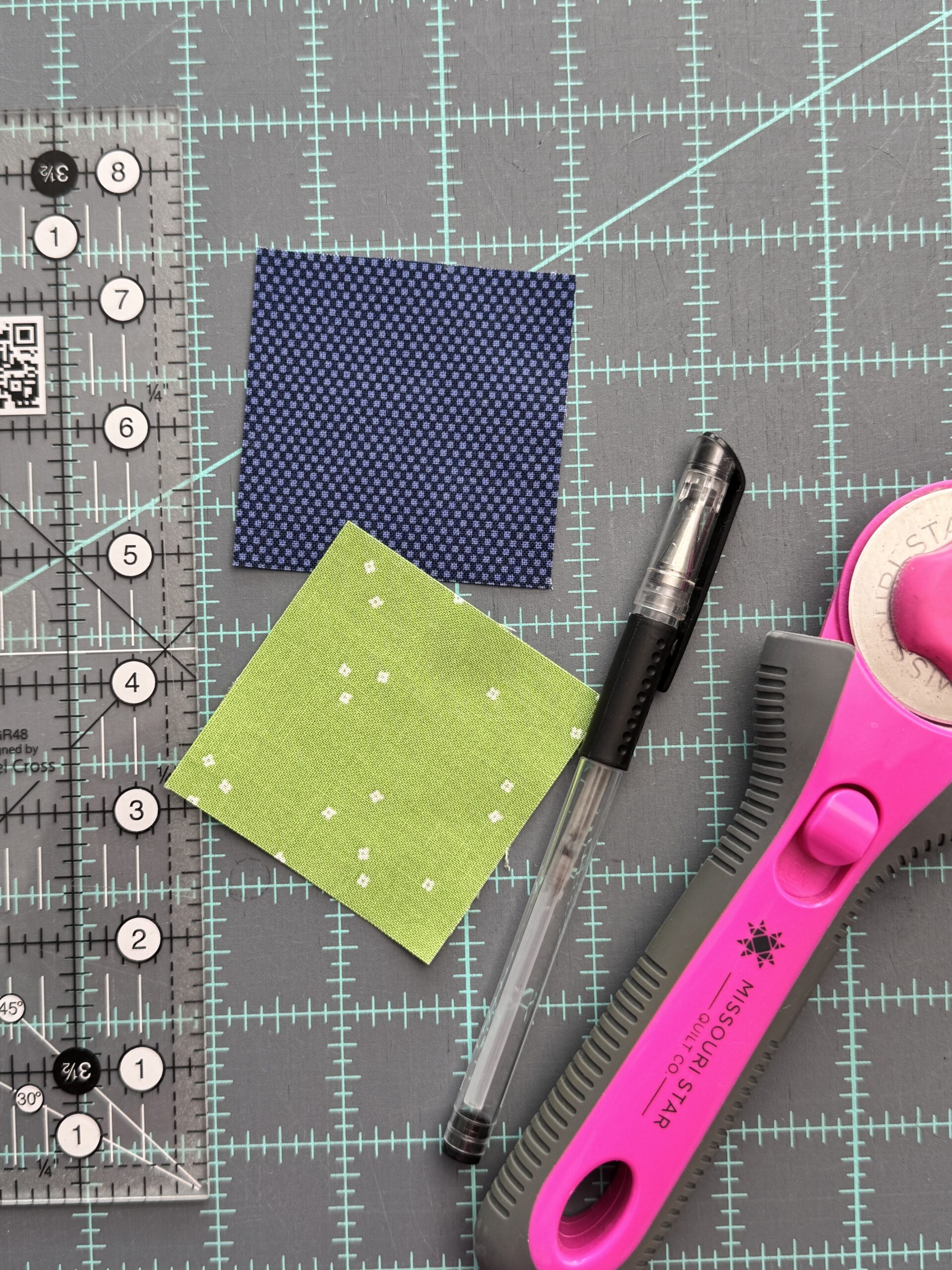 two 2.5 inch fabric squares with rotary cutter ruler and marking pen for half square triangles