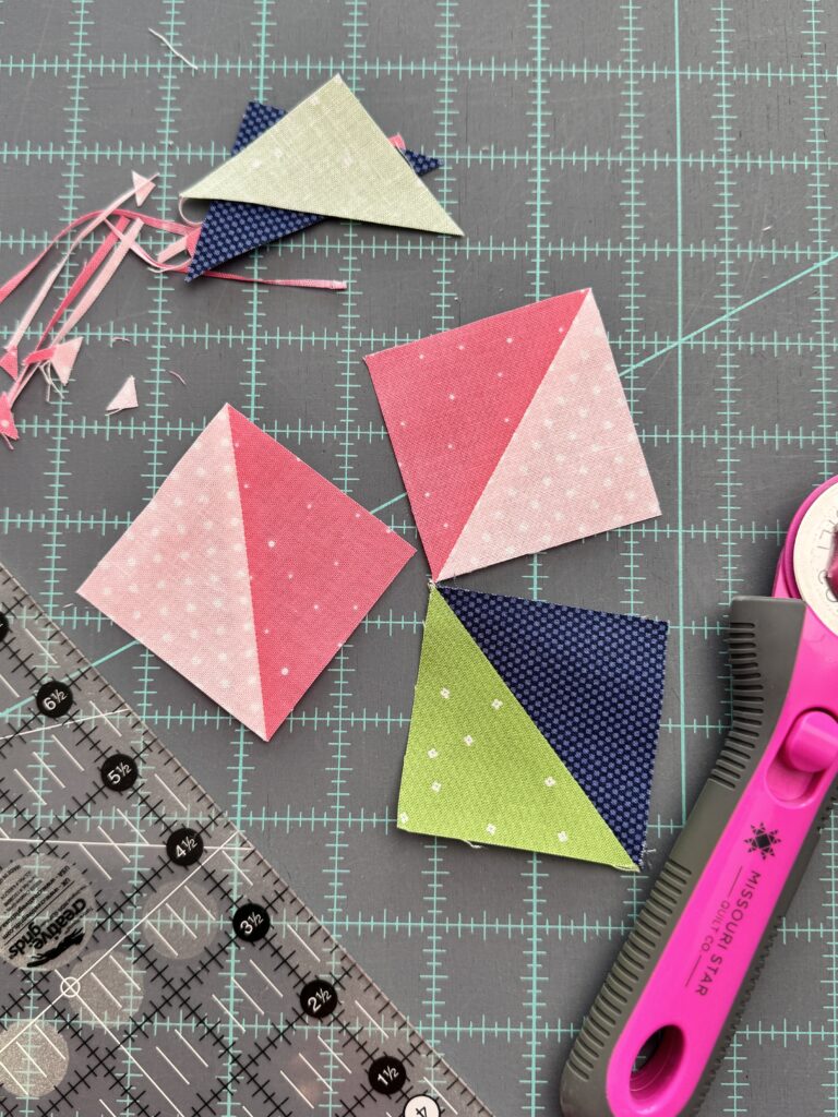 three finished half square triangles with trimming scraps rotary cutter and ruler