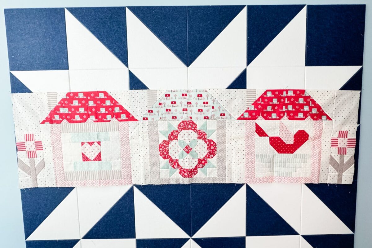The first row of the Designer Mystery 2024 block of the month quilt with three houses and two flower blocks for accent.