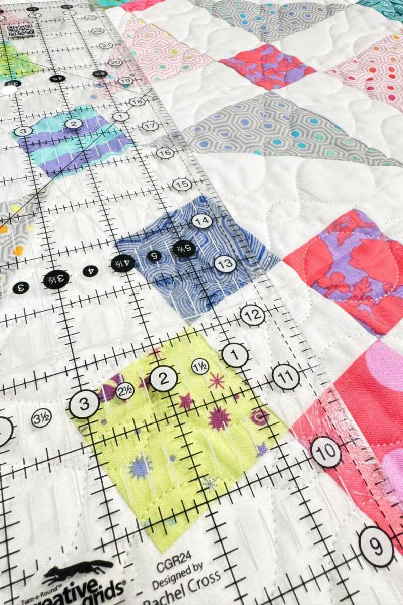 Close-up of a quilting ruler with grid lines on fabric, showing clear measurement markings and angles.