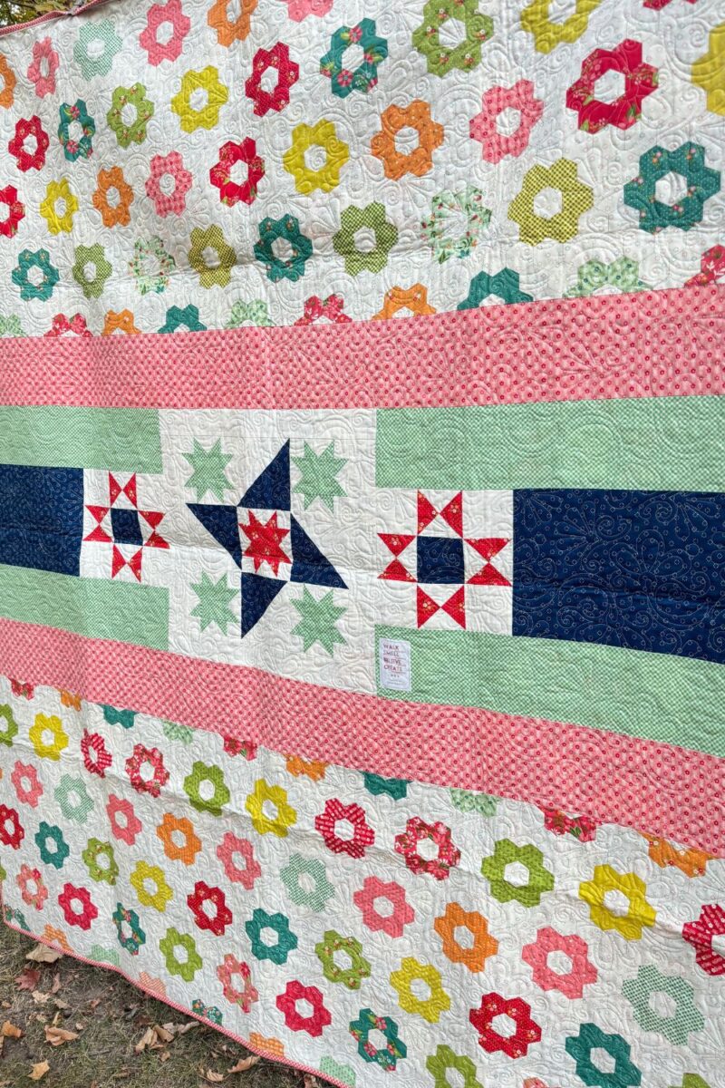 Back view of the Moonbeams Quilt, featuring a pieced backing made from the cheater panel and other fabrics from the Strawberry Lemonade collection
