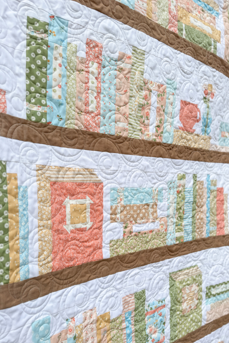 Angled view of a bookshelf quilt row with books and plant blocks in pastel colors.