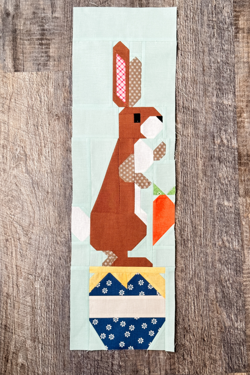 Finished Rabbit quilt block with Rabbit standing on a blue hunny pot holding a carrot.