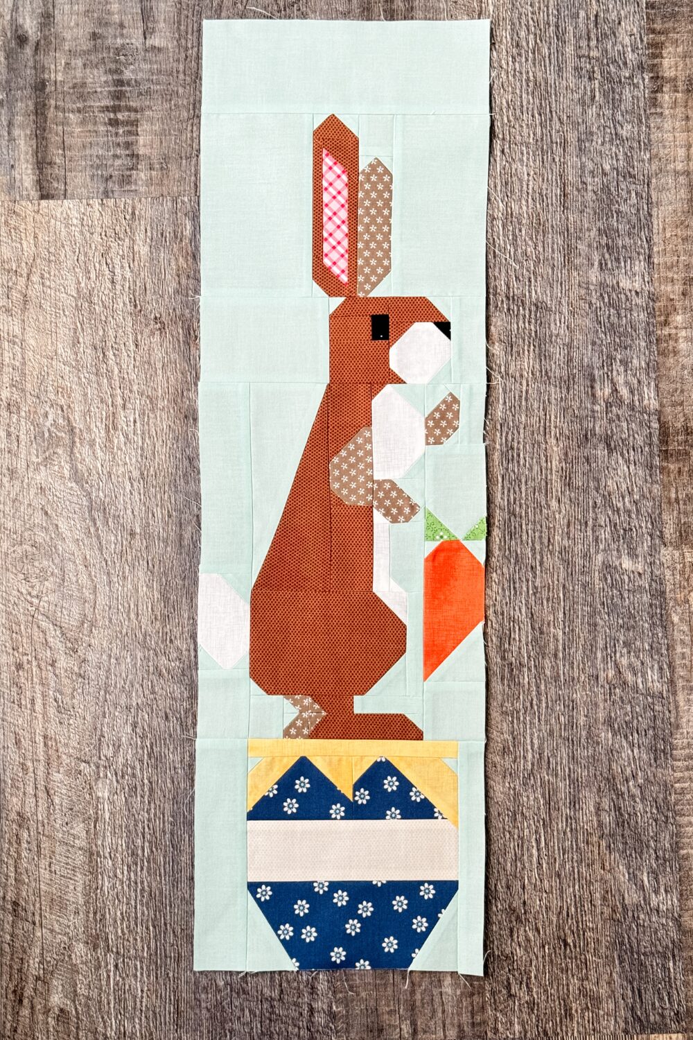 Finished Rabbit quilt block with Rabbit standing on a blue hunny pot holding a carrot.