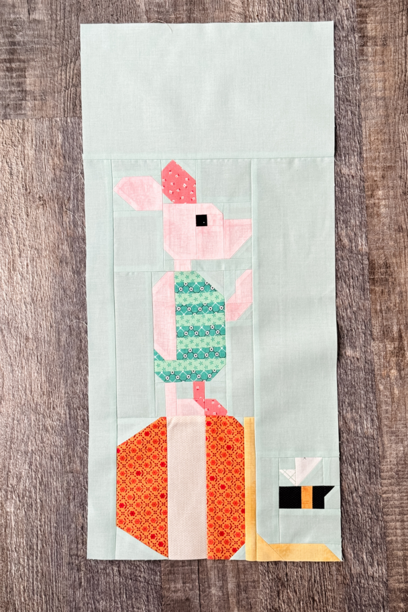 Finished Piglet quilt block with Piglet standing on a tipped over hunny pot and a flying bee.