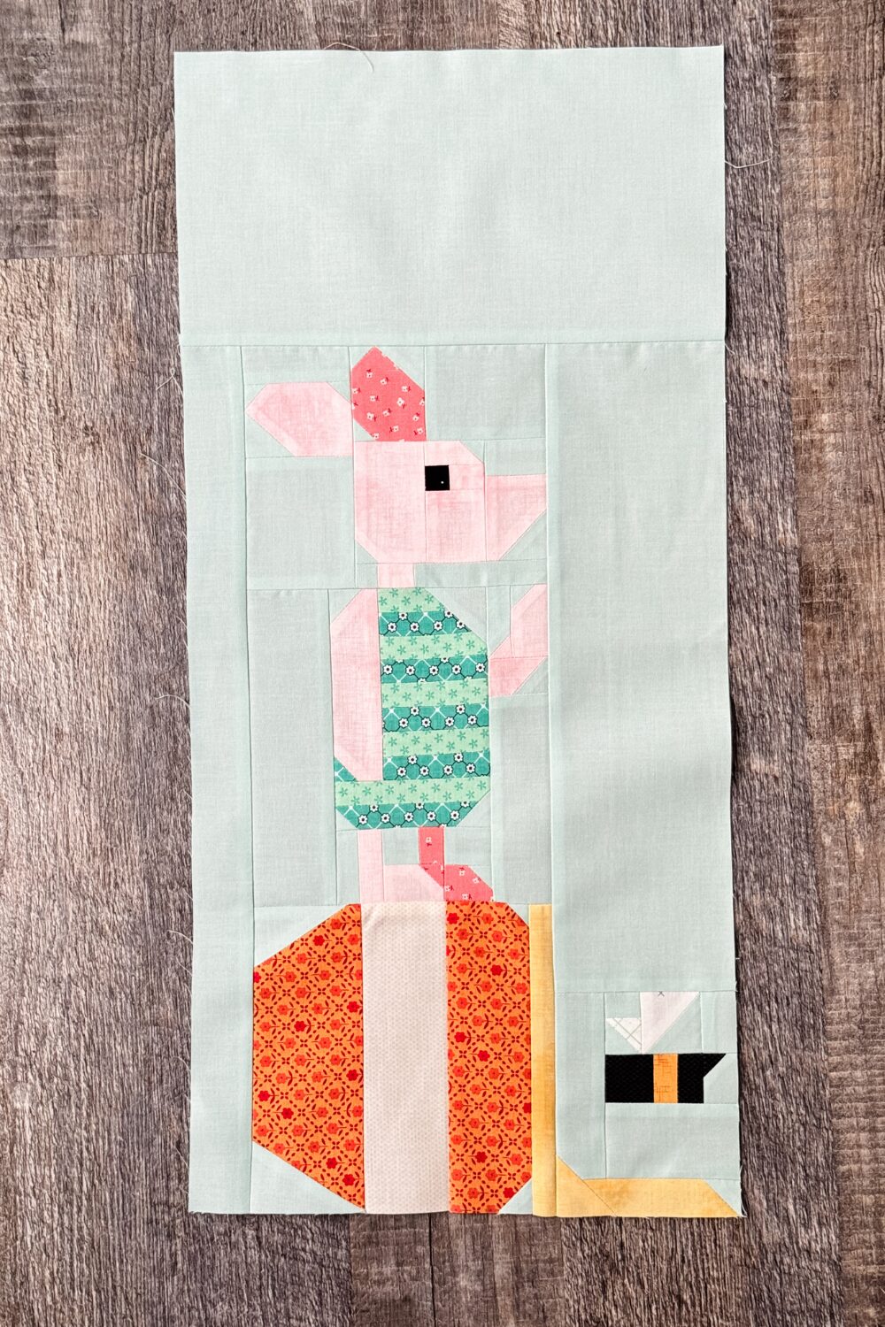Finished Piglet quilt block with Piglet standing on a tipped over hunny pot and a flying bee.