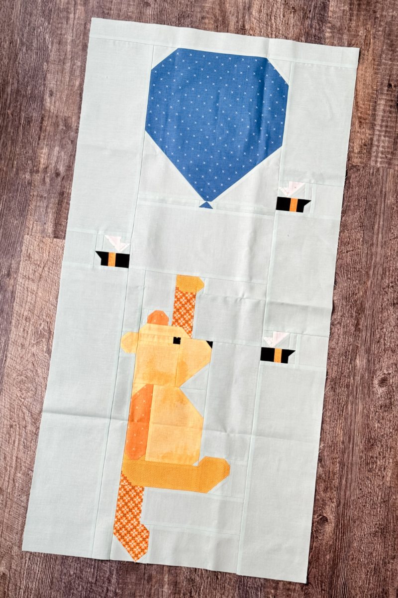 Completed Winnie the Pooh quilt block with Pooh holding a blue balloon and bees fluttering around.