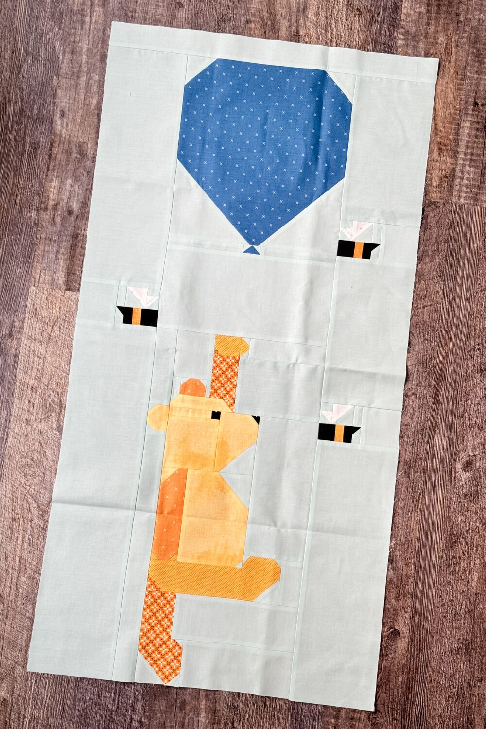 Completed Winnie the Pooh quilt block with Pooh holding a blue balloon and bees fluttering around.
