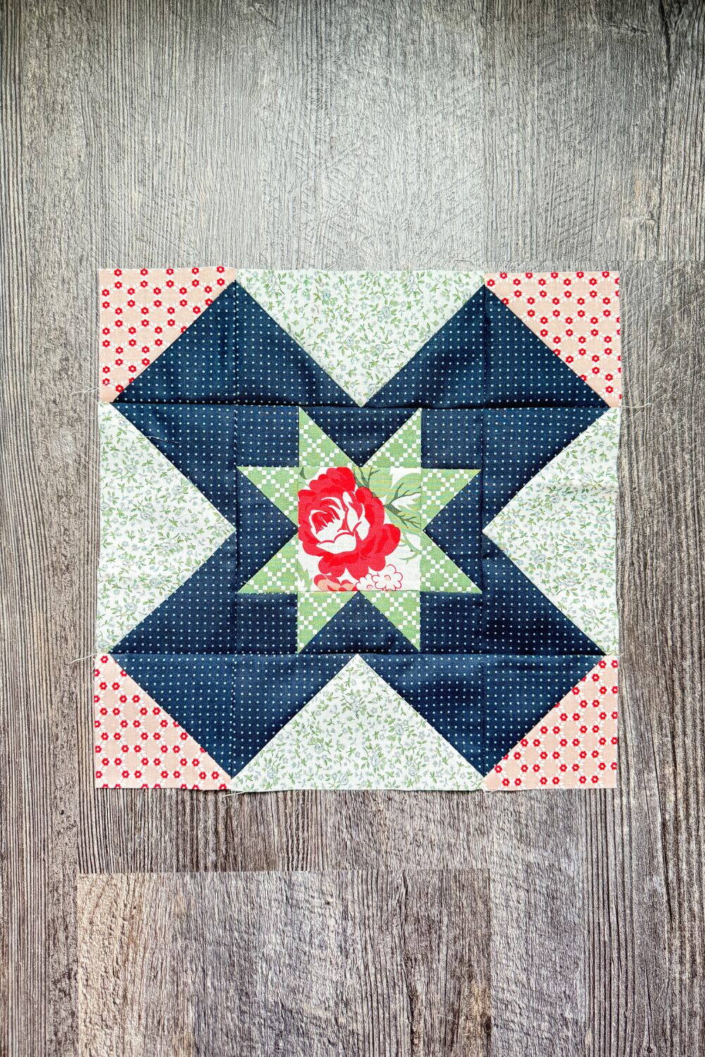 Eight Hands Around quilt block with fussy cut pink flower center and navy fabric creating an X shape.