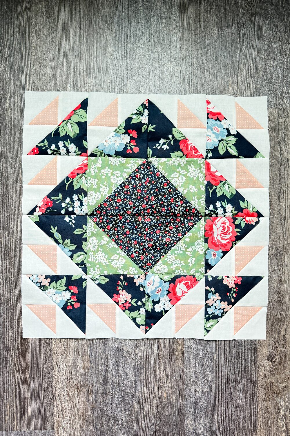 Four Aircraft quilt blocks sewn together with navy floral fabric surrounding a green and navy floral center.