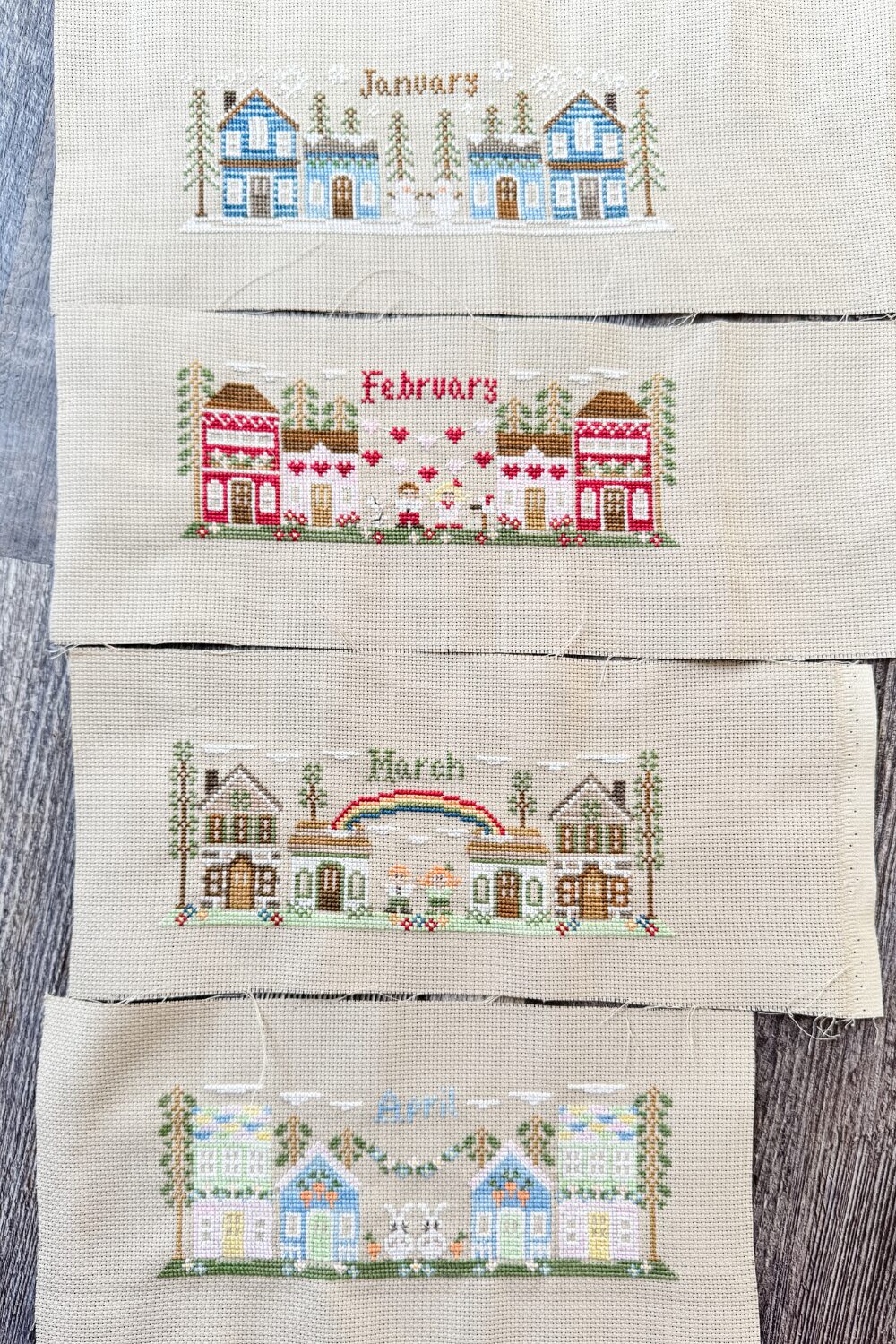 Cross stitch designs for January to April from the Monthly Mini Village series by Country Cottage Needleworks, ready for finishing into pillows.