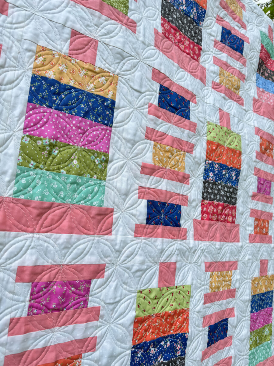 Close-up of Orange Dream quilting pattern on the Strippy Spools quilt featuring bobbin and spool blocks.