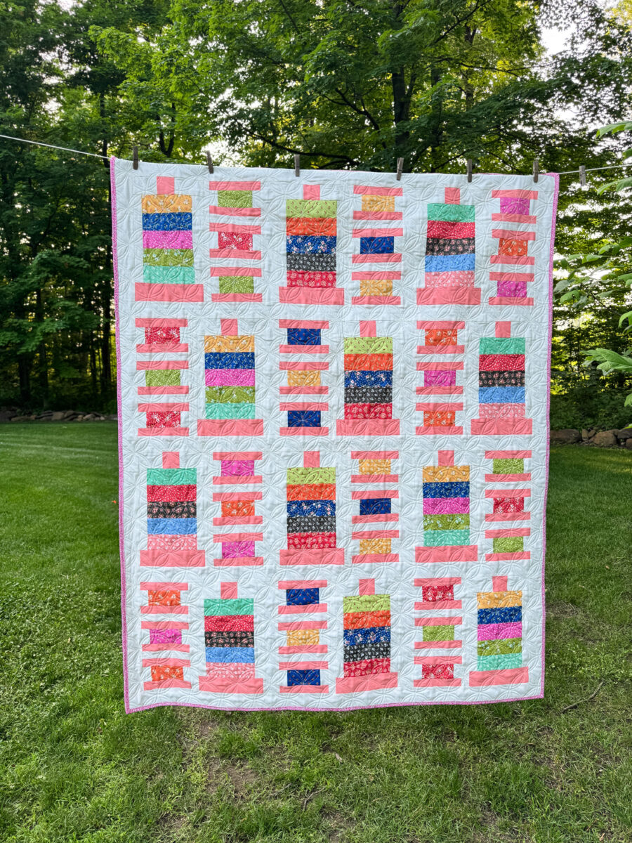 Full view of the finished Strippy Spools jelly roll quilt with spool and bobbin blocks made from Cali & Co jelly roll and white background.