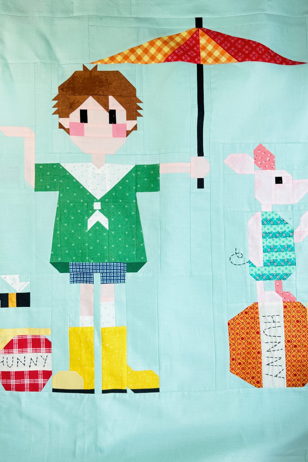 A quilt block of Christopher Robin holding an umbrella over Piglet who is standing on a honey pot.
