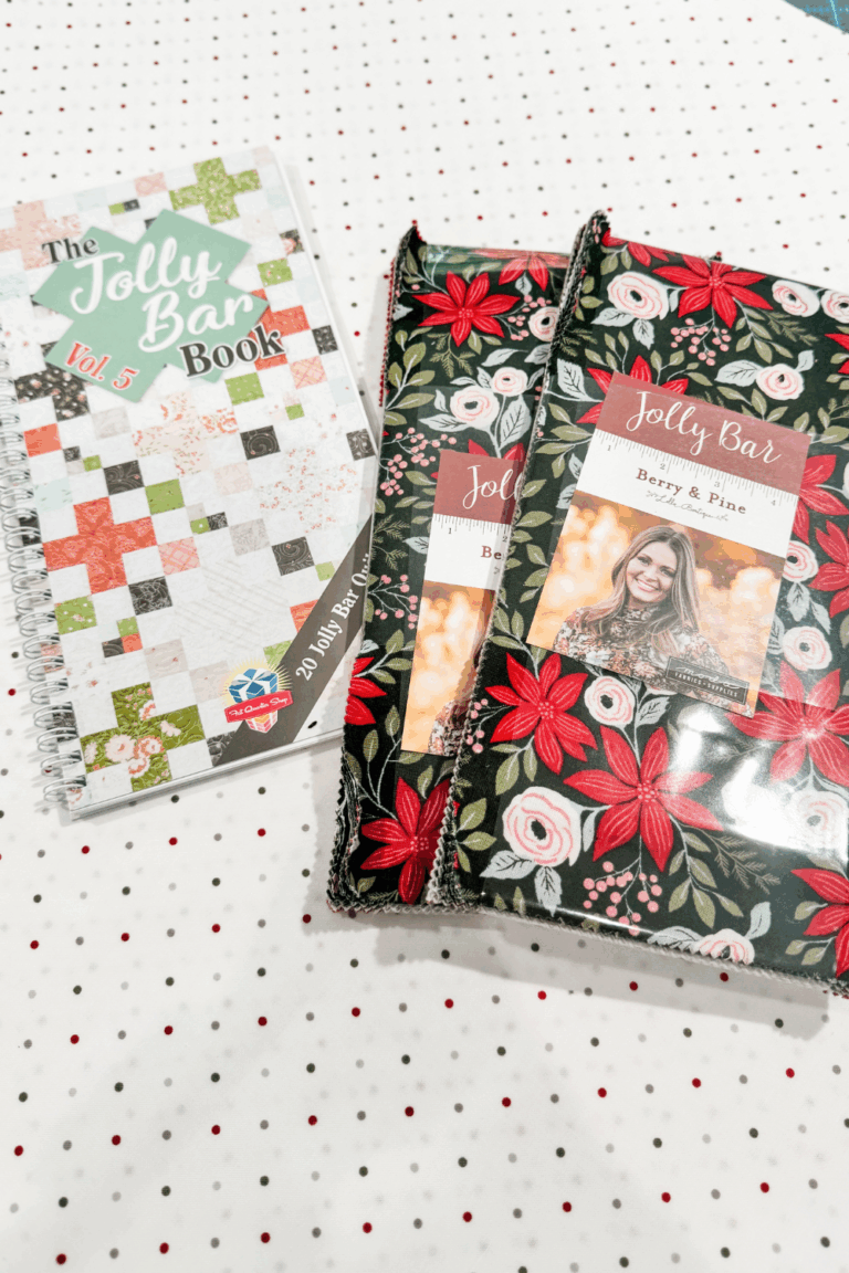 Close-up photo of Berry & Pine Jolly Bars, Jolly Bar Volume 5 book and Magic Dog Christmas fabric.