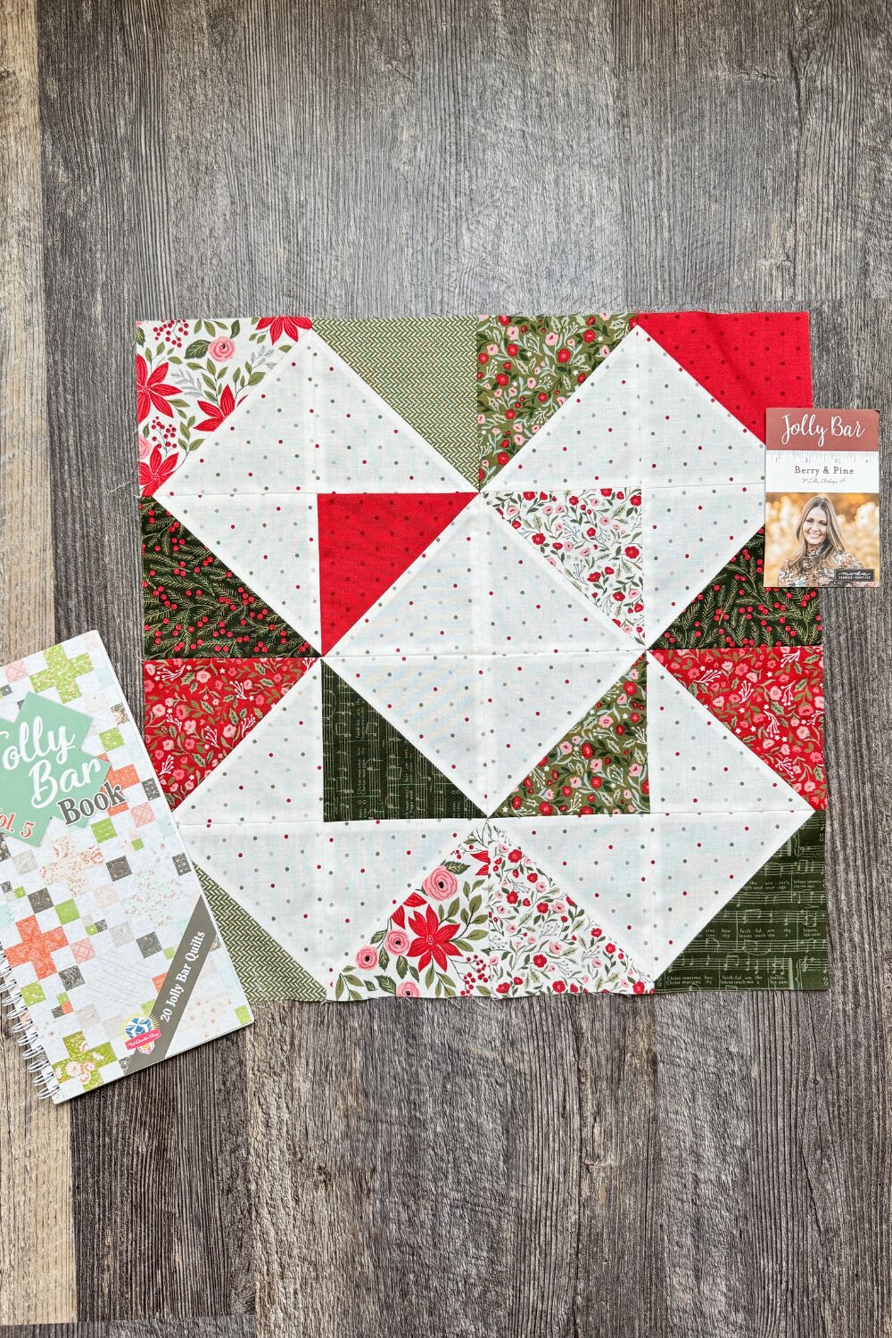 Completed Refractions quilt block pictured with a Jolly Bar volume 5 book. Made with Berry and Pine fabrics.