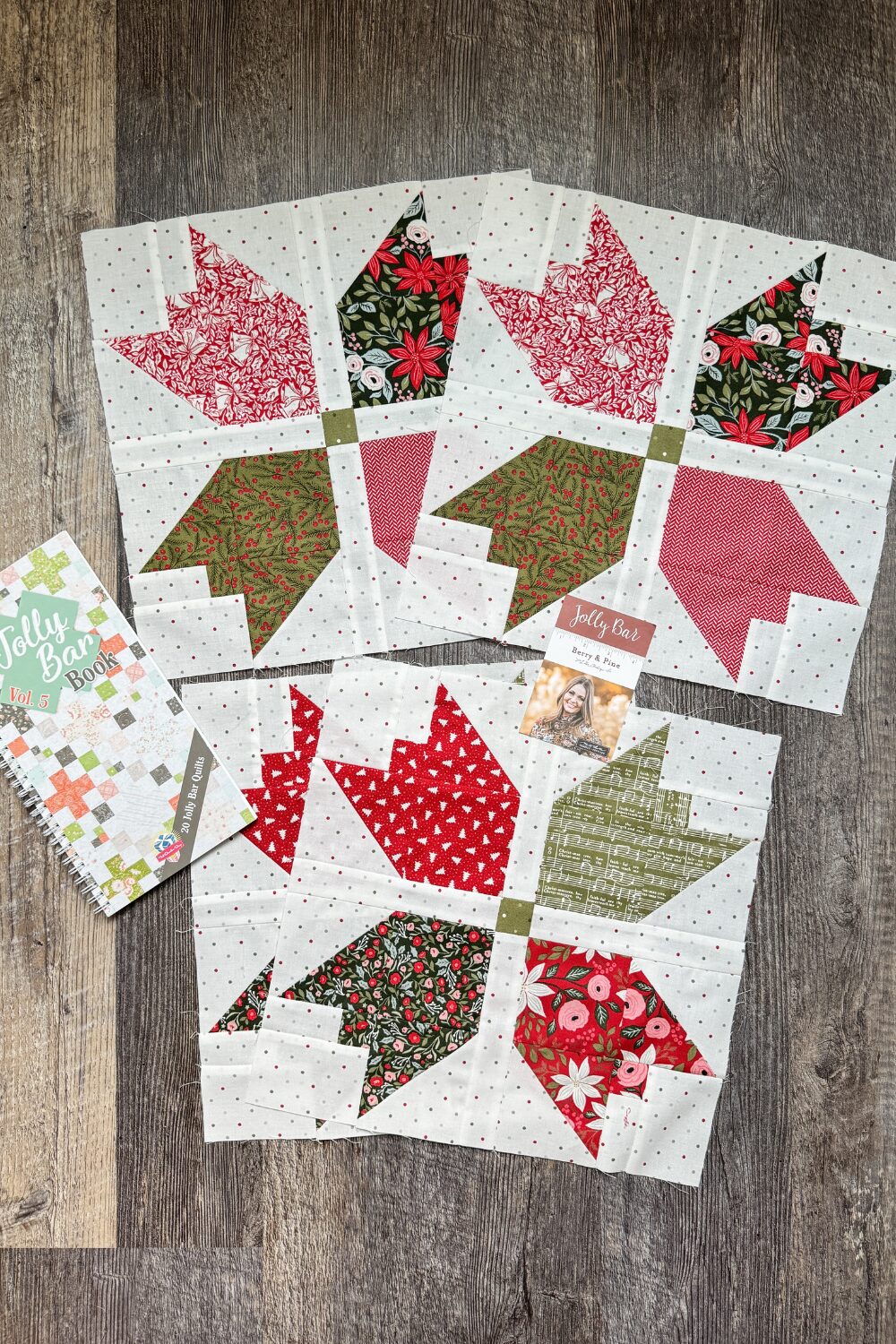 The four Holly Berry quilt blocks flat lay with the Jolly Bar volume 5 quilt book.