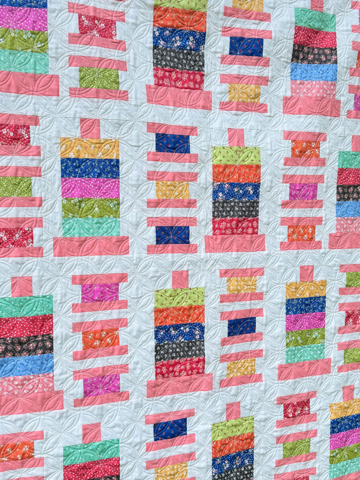 Side view of Strippy Spools quilt made with Cali & Co fabric and coral Bella Solid spools, hanging outdoors in natural light.