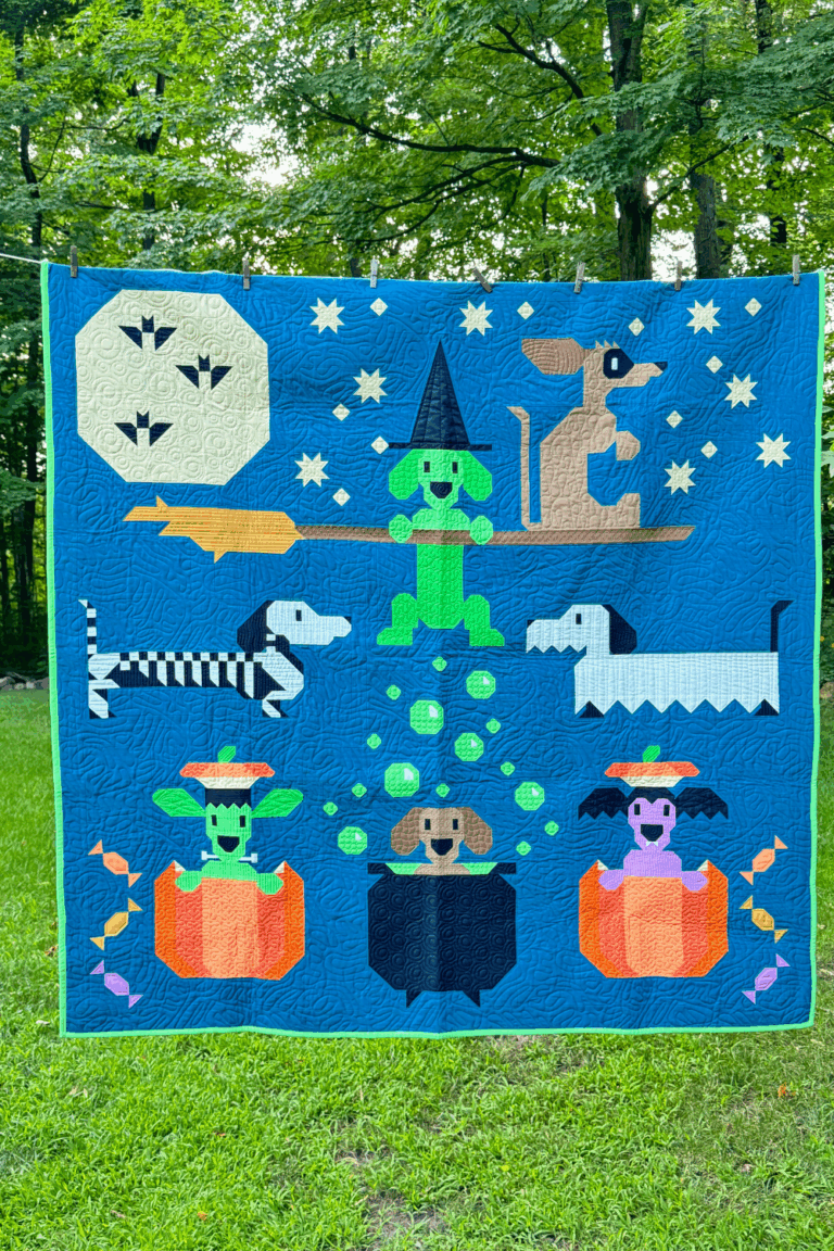 Full view of the Halloweenies Quilt by Art East Quilting Co., featuring seven weiner dogs in Halloween costumes with moon, bats, and pumpkins.