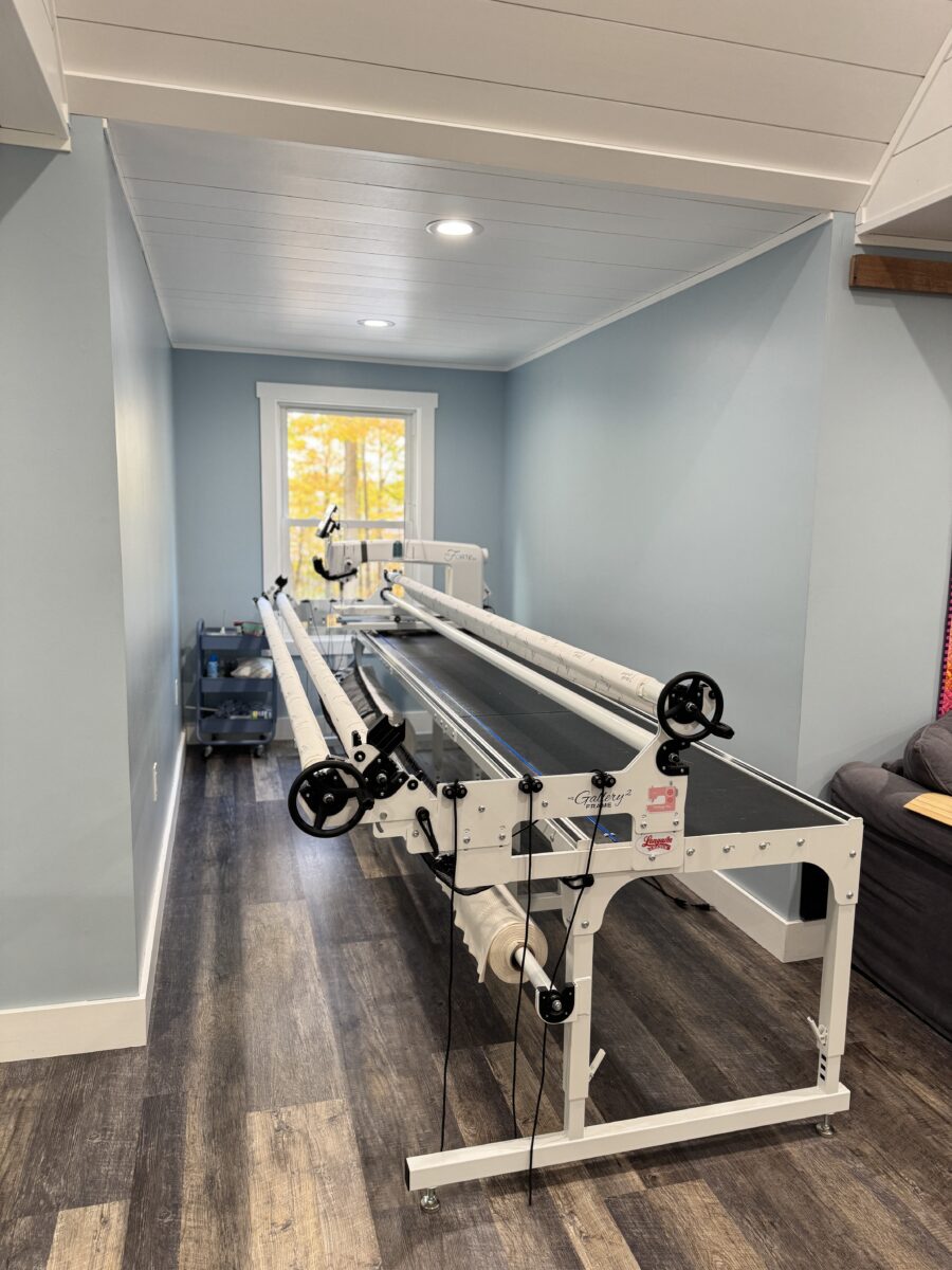 Longarm quilting machine with a rolling cart filled with threads and accessories.