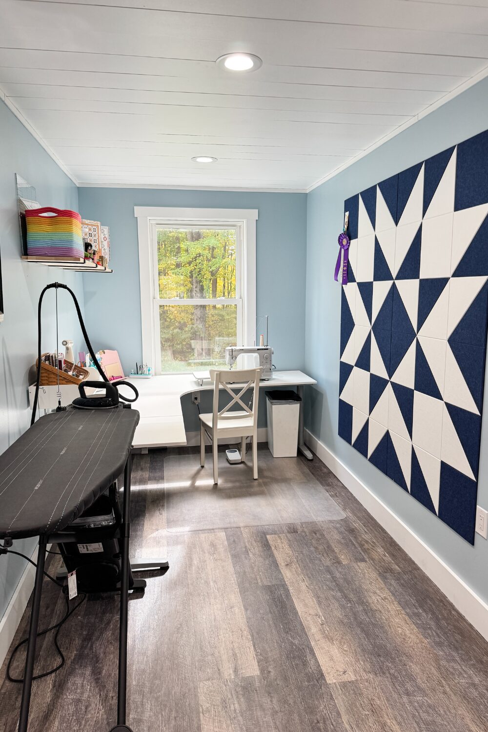 L-shaped desk with a Juki sewing machine, wall-mounted design board, and LauraStar ironing system.