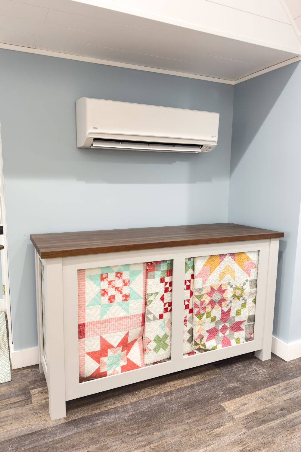 Wall-mounted mini split HVAC above a large handmade quilt storage cabinet.