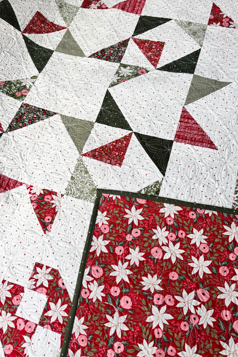Red floral quilt backing folded over the front of the Jolly Bar 5 sampler quilt.