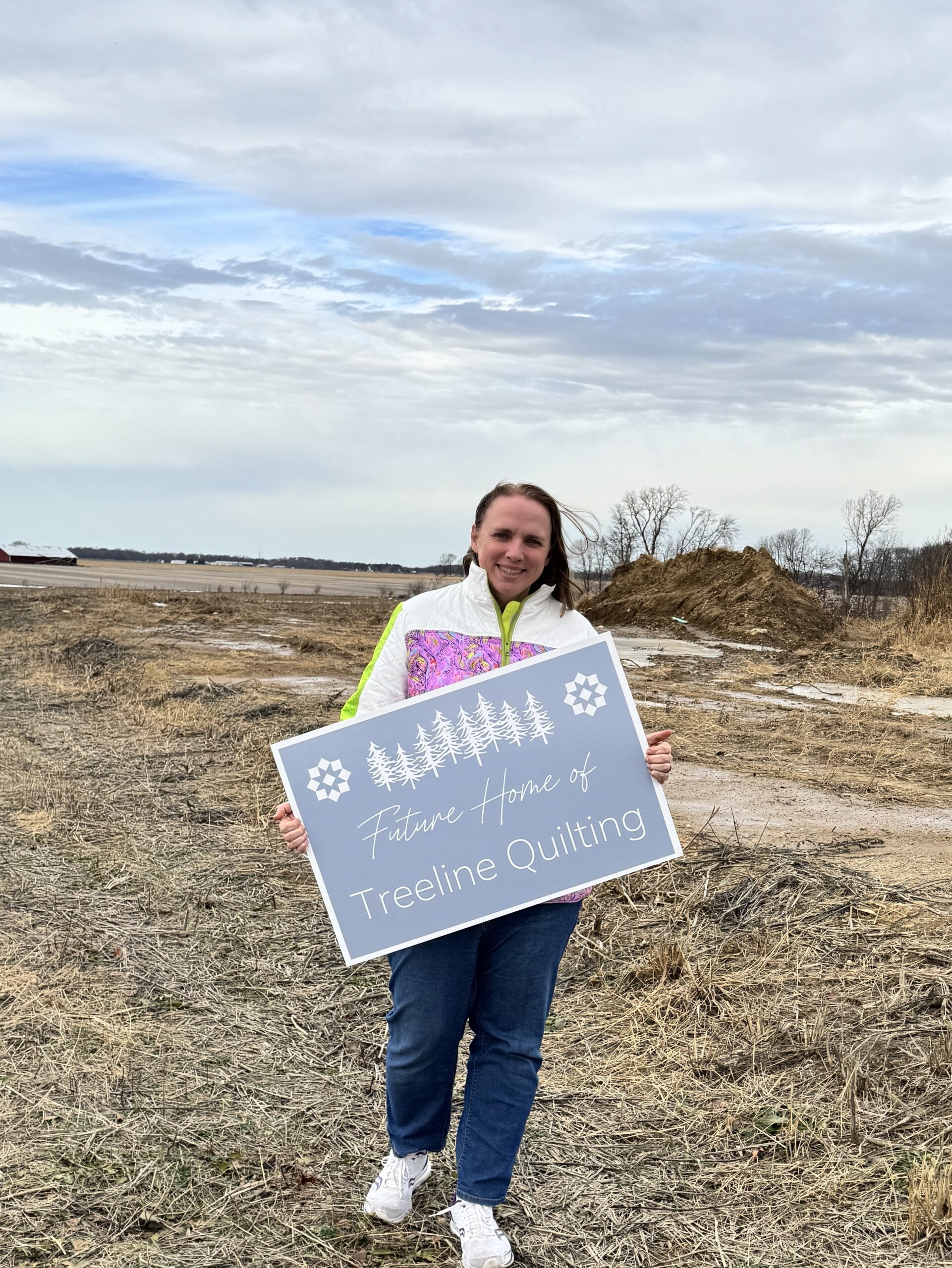 Image of Nicole holding a Future Home of Treeline Quilting sign at the build site. 