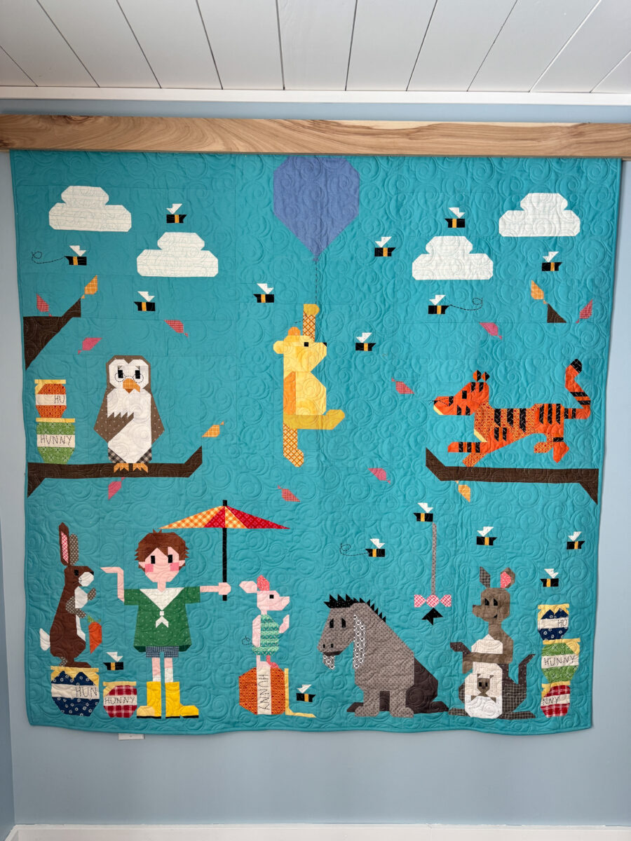 Full view of the smaller Winnie the Pooh quilt hanging on the wall.