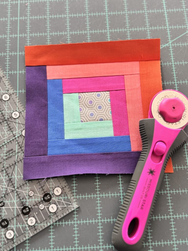 Finished log cabin quilt block in bright solids with a quilting ruler and rotary cutter.