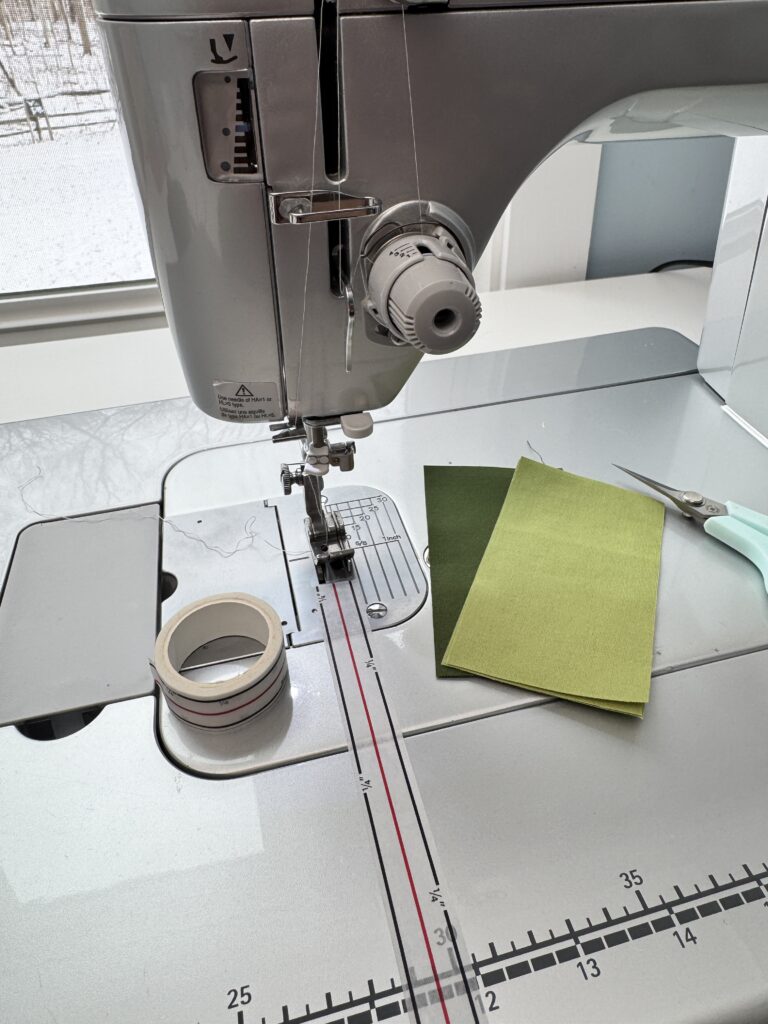 Sewing machine with quarter inch foot attached. Roll of Diagonal Seam Tape is also applied to the bed of the machine for an accurate quarter inch seam