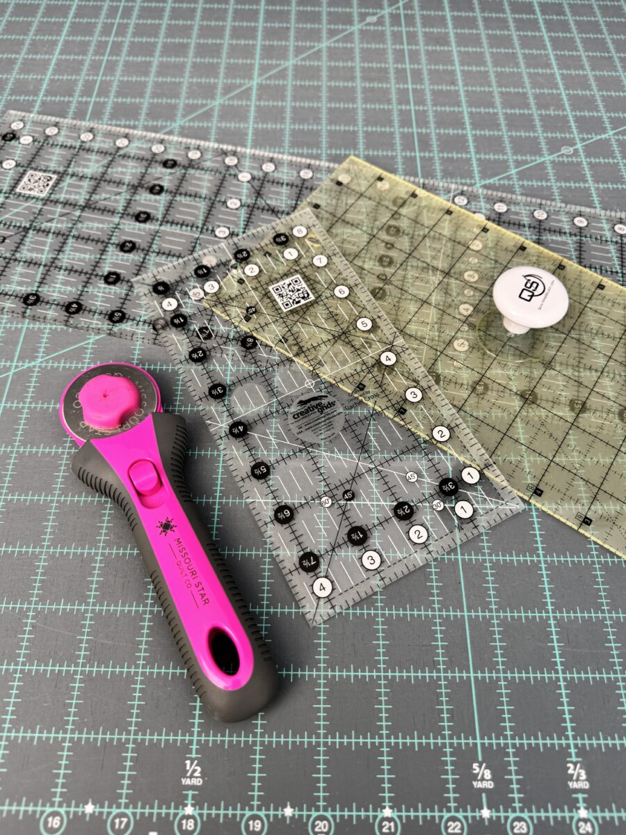 A pink rotary cutter and three rectangle cutting rulers on a blue cutting mat.