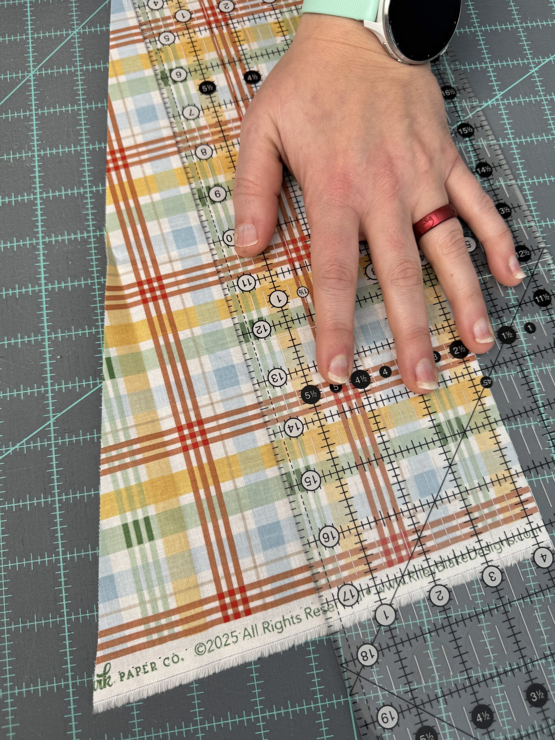 Proper hand positioning on a long acrylic quilting ruler. Hand is flat with pressure through the fingers. Hand is aligned in the center with pressure close to the cutting edge but with fingers safely out of the way. This method will increase the likelihood of accurate cutting for quilting